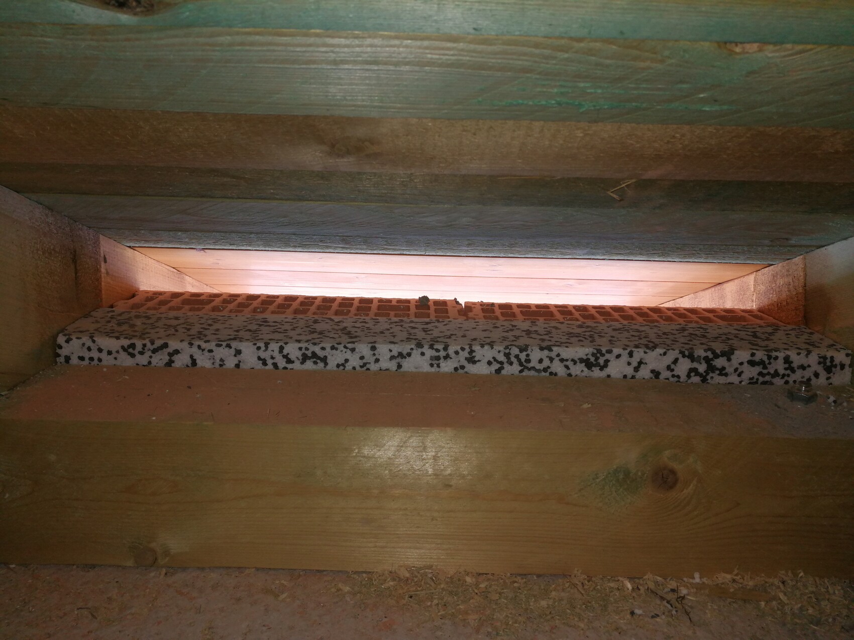 Unterbau aus Holz: lange perforierte weiße Dämmplatte mit schwarzen Flecken liegt zwischen Balken.