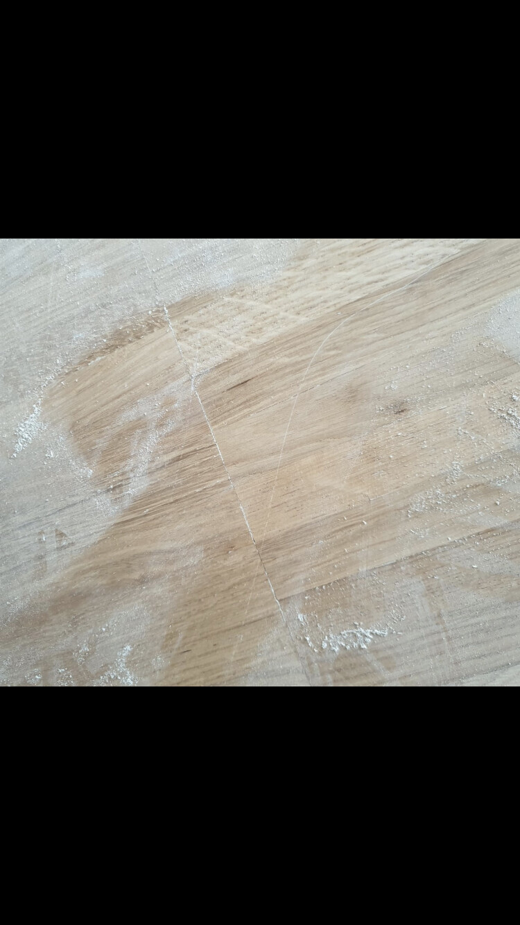 Holzboden mit Staub- und Mehlresten; eine diagonal verlaufende Holznaht sichtbar.
