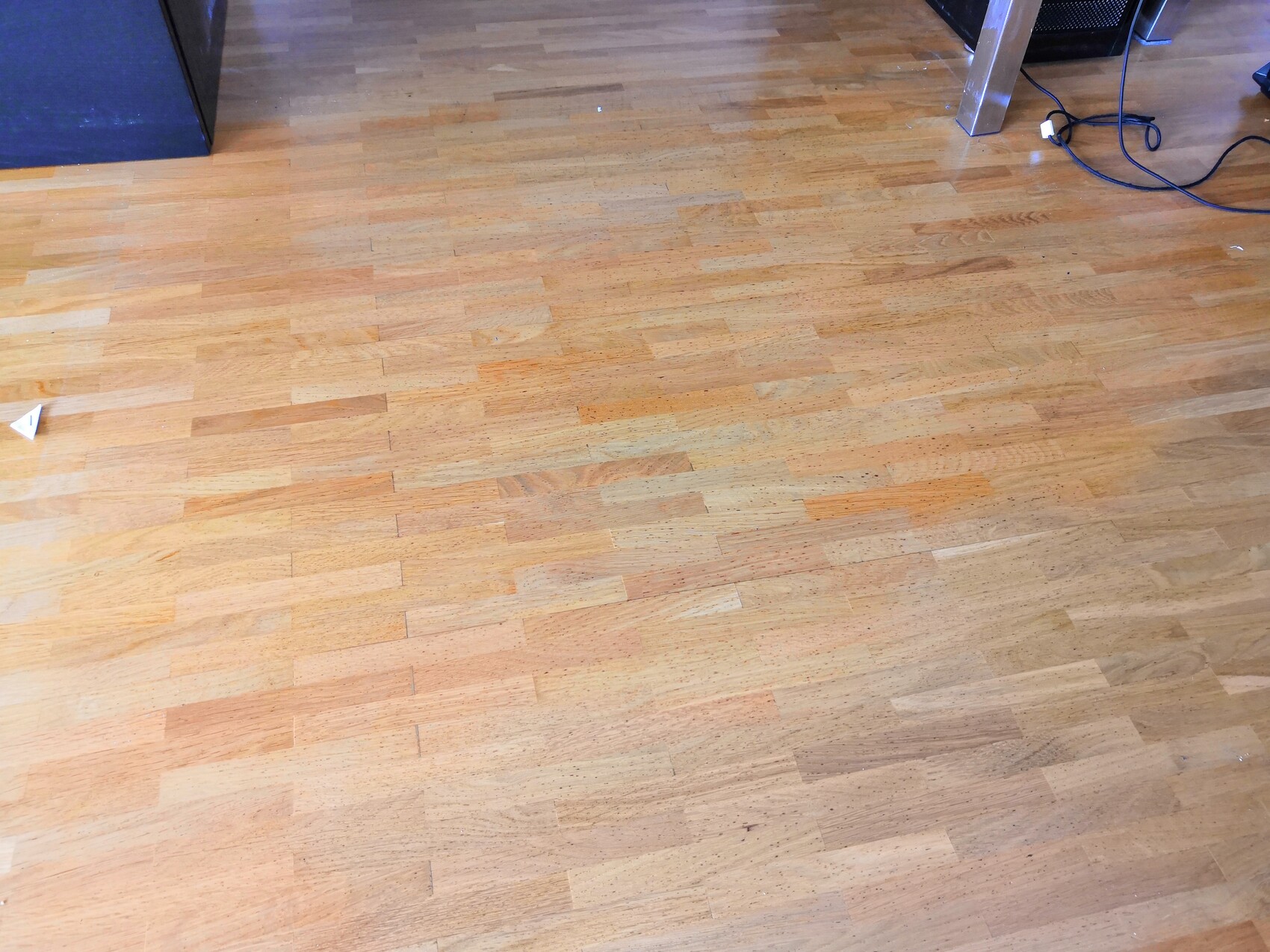 Heller Holz-Parkettboden, rechts Kabelreste, oben rechts Tischbein, links kleines Papier.