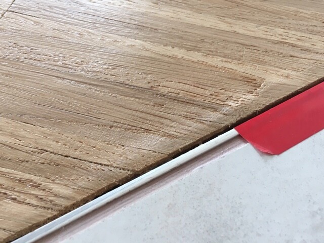 Holztischplatte mit Holzmaserung; rote Kante eines Gegenstands liegt auf weißem Untergrund.