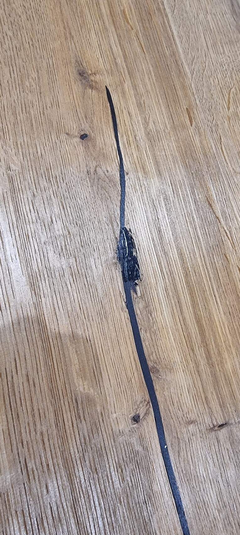 Holzfußboden mit einer langen dunklen Rissfuge; in der Mitte klebriges schwarzes Material.
