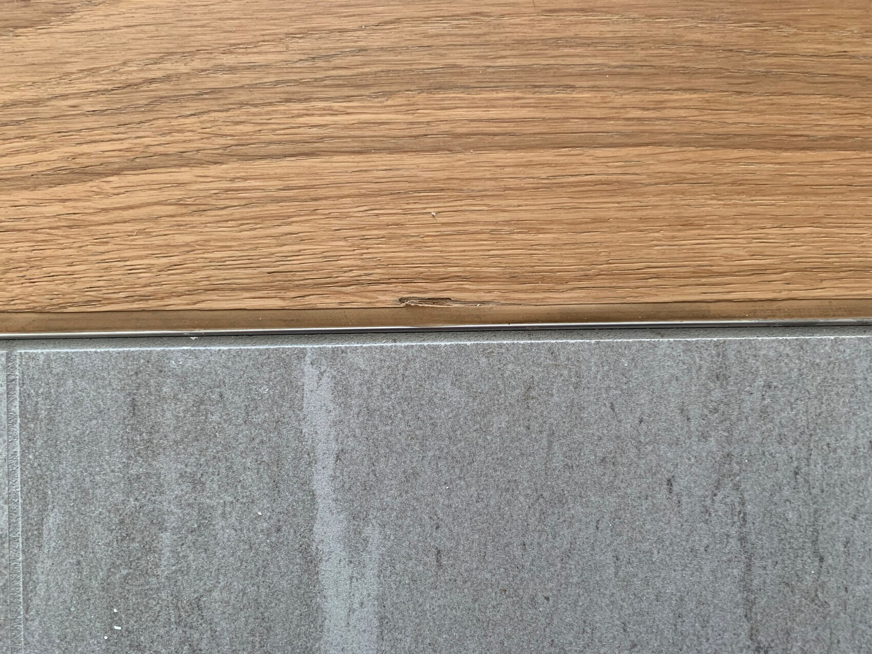 Übergang Holzboden oben zu grauem Boden unten, Metallkante am Rand.