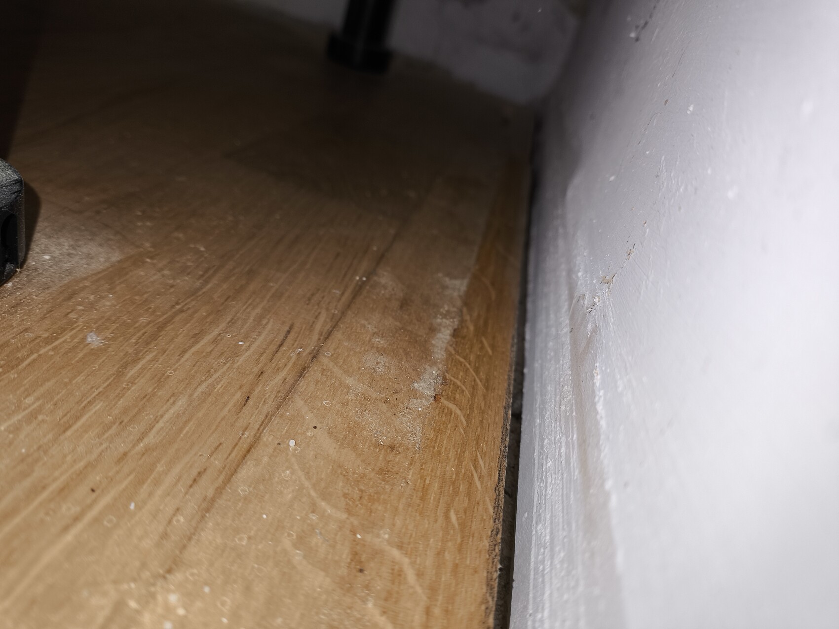 Nahaufnahme eines Holzfußbodens im Innenraum nahe der weißen Wand mit Staubkörnchen.