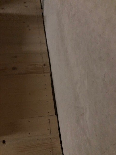 Holzfußboden links, helle Wand rechts; Ecke zwischen Boden und Wand.