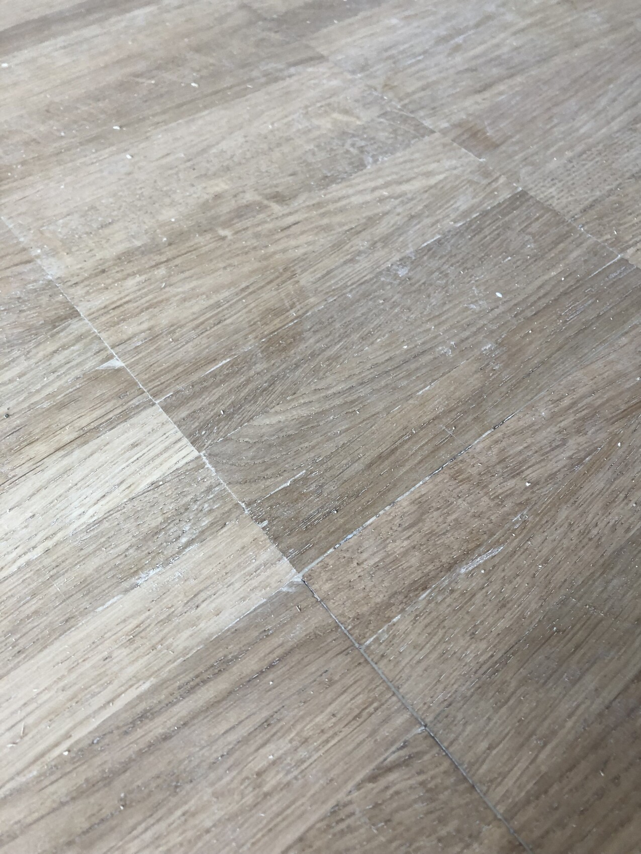 Holz- oder Laminatboden mit sichtbaren Fugen, Staub und leichten Kratzern.
