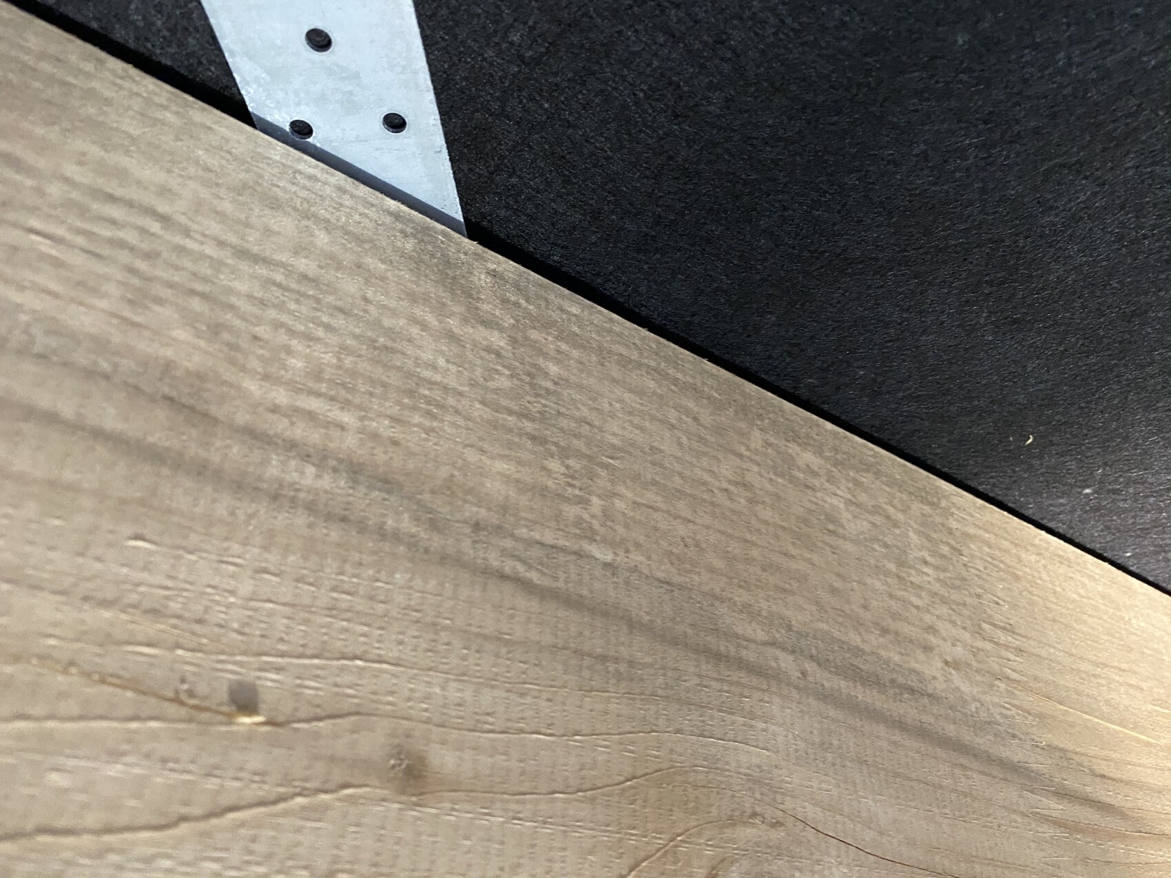 Nahaufnahme eines Holzbretters am unteren Rand, schwarzer Hintergrund, Metall-L-Winkel mit Schrauben