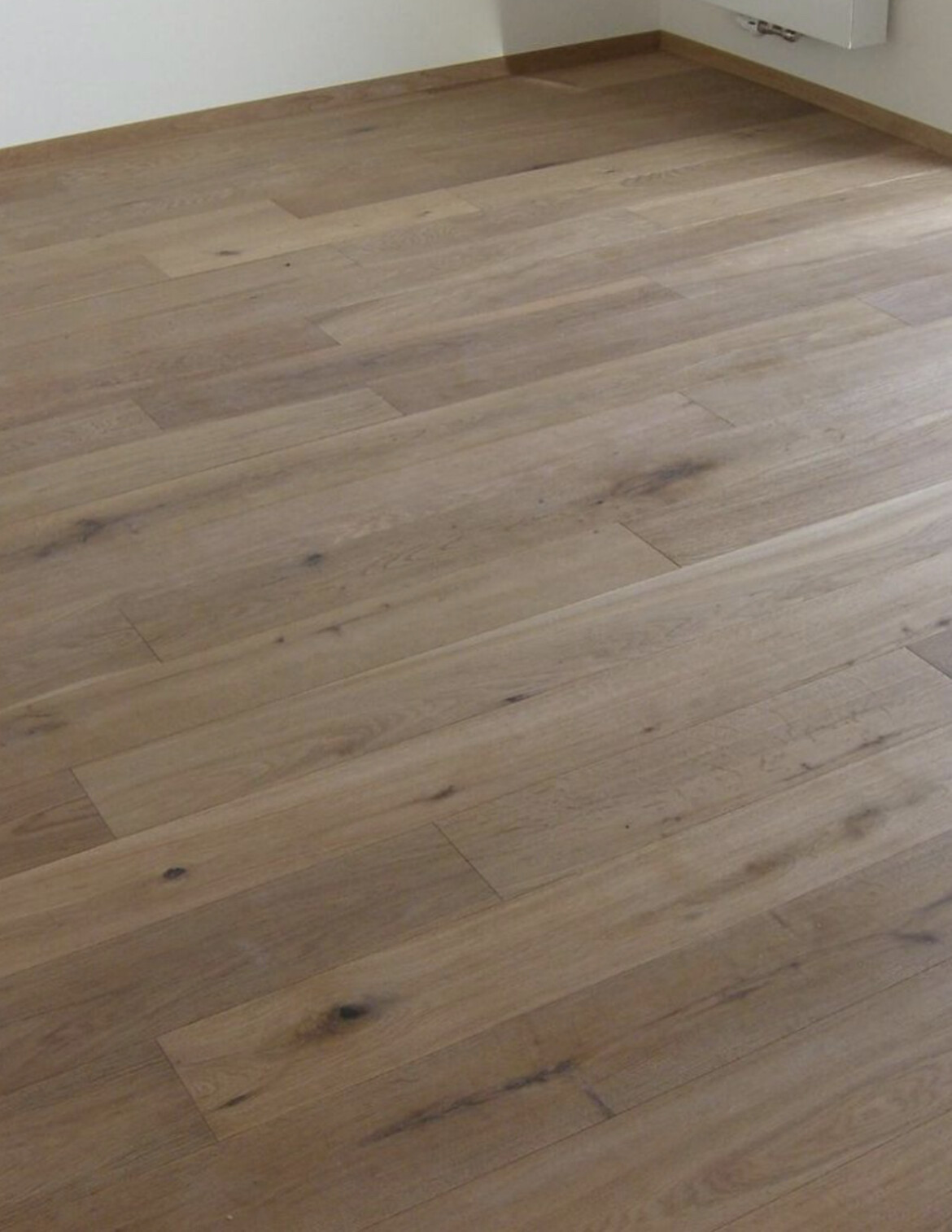 Holzboden aus Eichenholz im Zimmer mit sichtbarer Maserung, Flecken und Knoten.