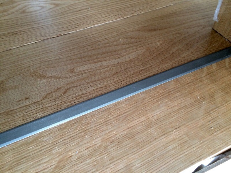 Holzparkett mit einer schmalen metallischen Übergangsleiste am Boden.