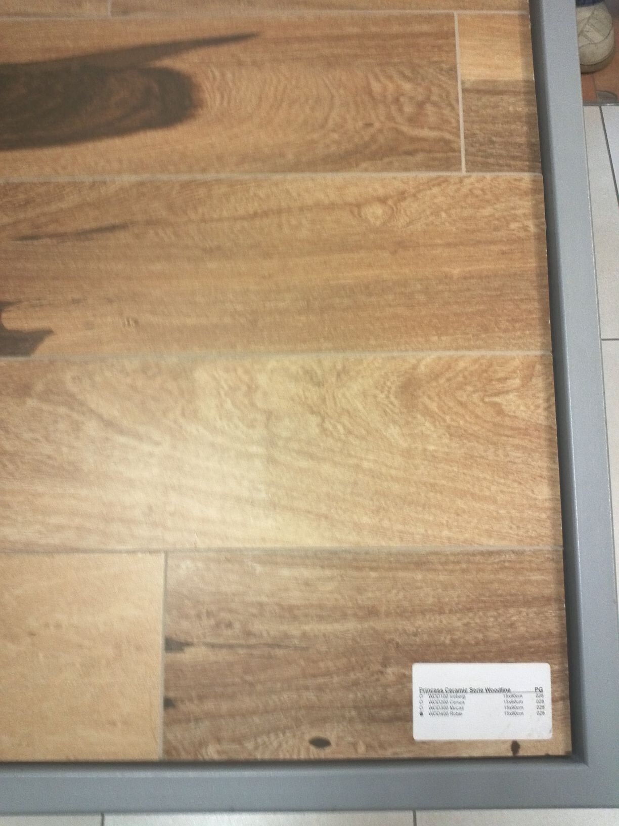Holzoptik-Fußboden mit braunen Laminatdielen, grauem Rahmen und kleinem Etikett unten rechts.