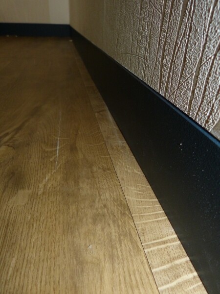 Nahaufnahme eines Holzfußbodens mit schwarzer Bodenleiste in einem Innenraum