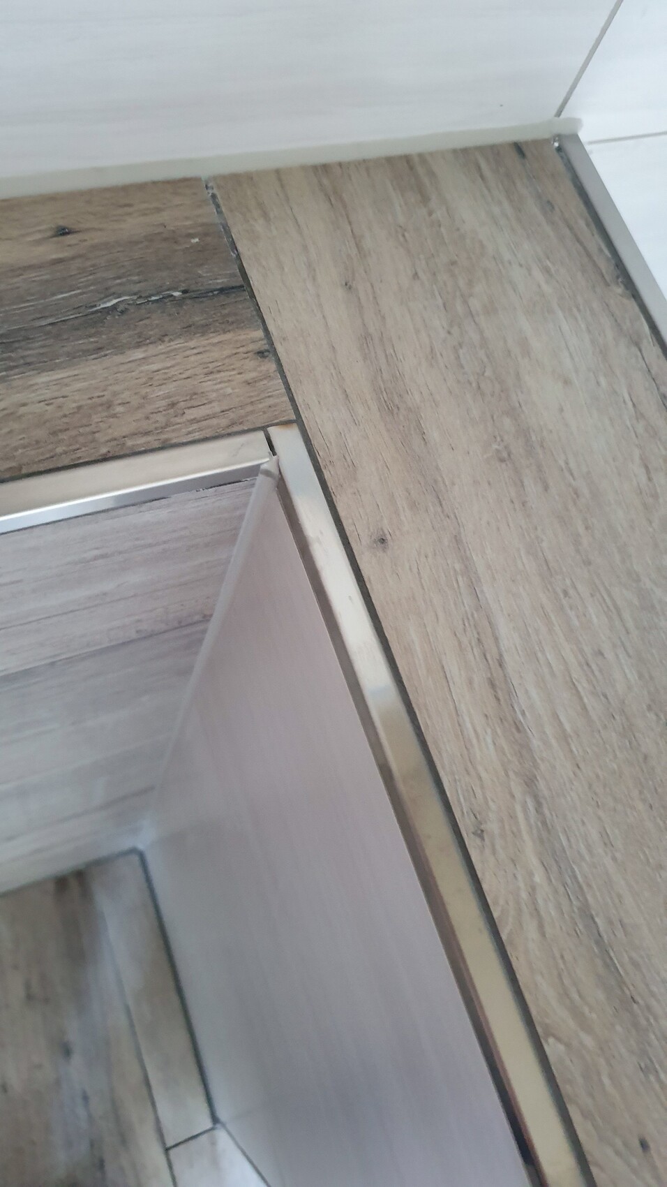 Eckansicht: Holzbodenplatten und eine silberne Metallkante einer Türfront.