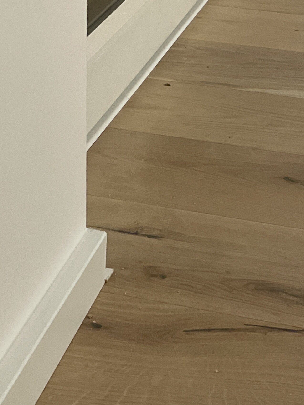 Ecke eines Raumes: weiße Wand mit Sockelleiste und brauner Holzboden mit Kratzern.