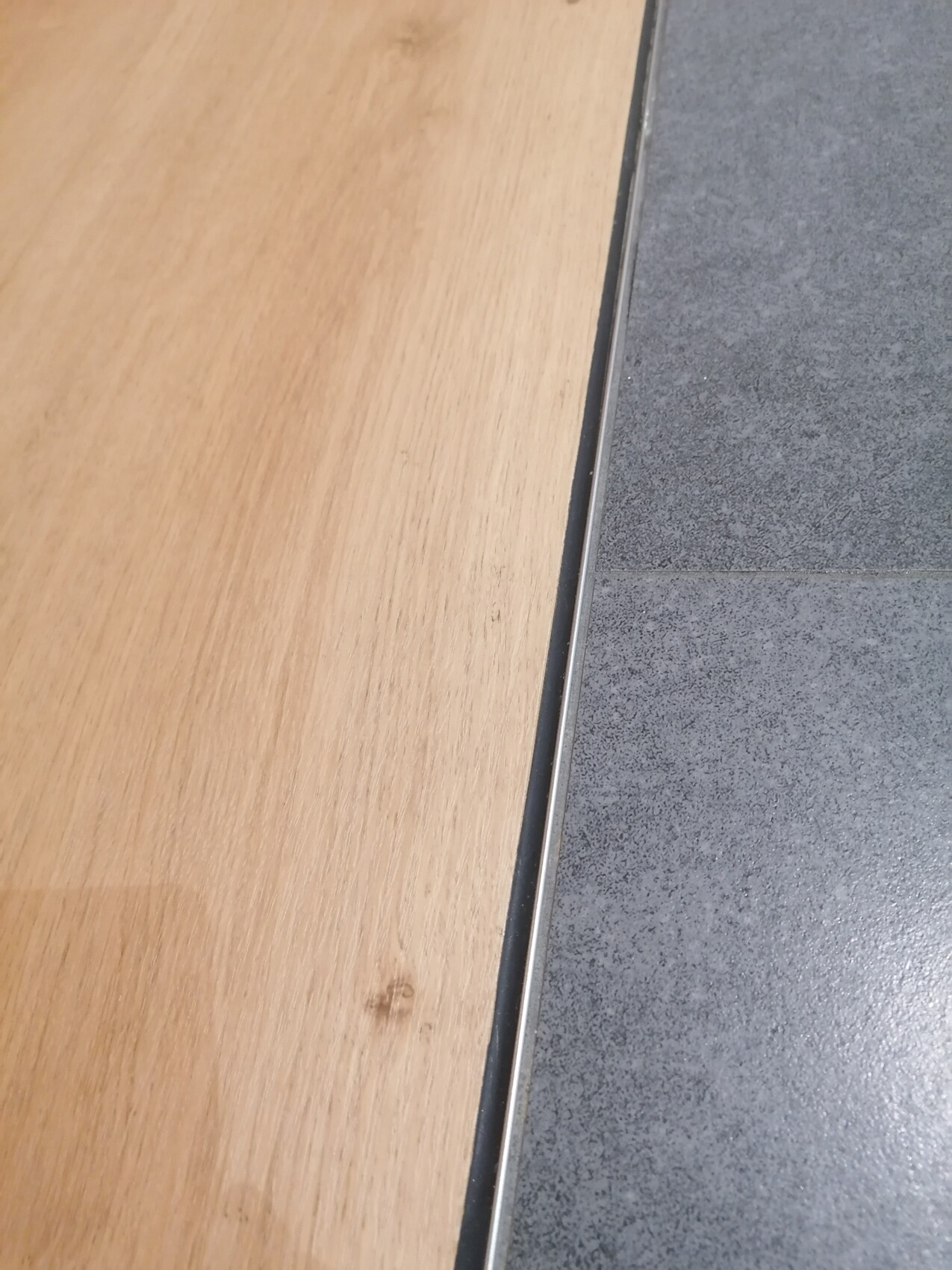 Übergang zwischen Holzboden links und grauen Fliesenboden rechts, Metallkante.