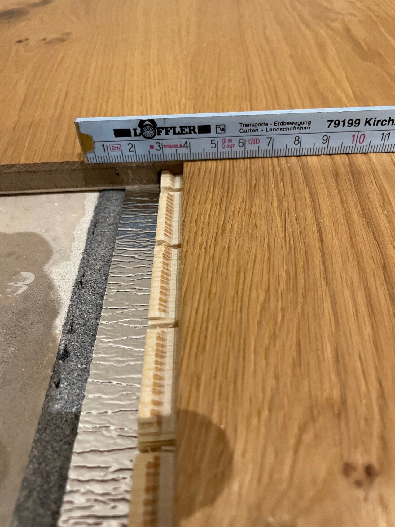 Messlatte (Löffler) über Holzboden; Holzkeile neben Untergrund aus Beton/Styrofoam.