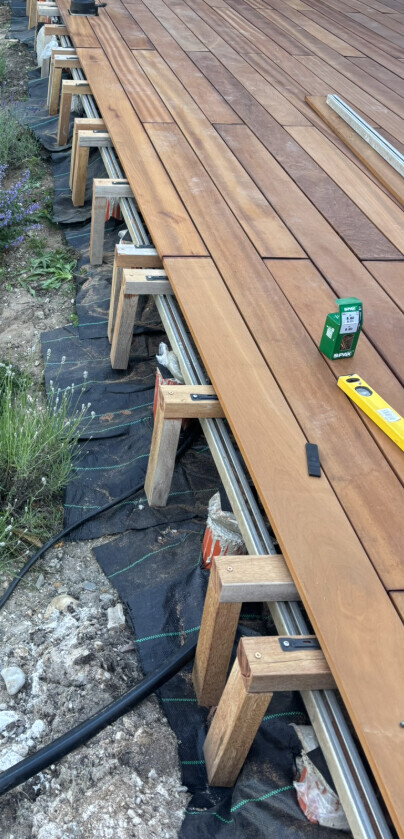 Holzdeck im Bau: Unterkonstruktion aus Balken, verlegte Deckbretter, Level und Werkzeug darauf.