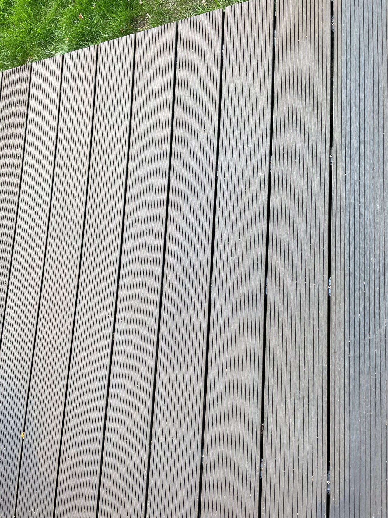 Dunkle Holzdeck-Dielen verlaufen parallel; Gras am oberen Rand sichtbar.