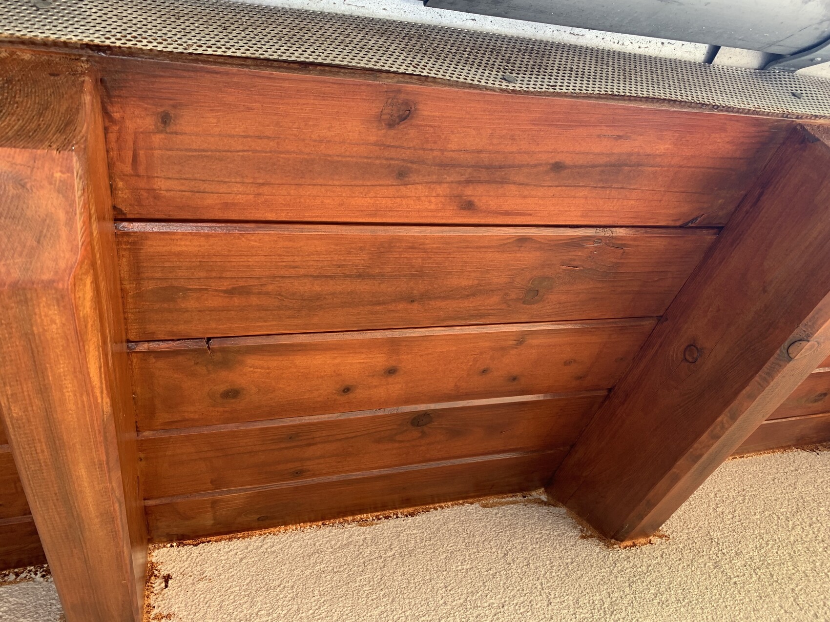 Unterseite eines braun gestrichenen Holzdecks mit seitlichen Pfosten und Metallgitter.
