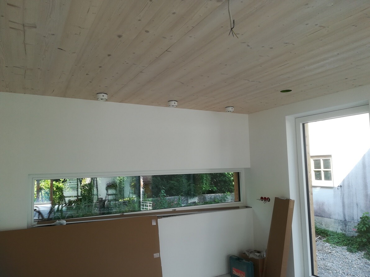 Innenraum im Bau: Holzdecke, lange Fensterfront, Bauteile/Werkzeugstapel, Makita-Kasten.