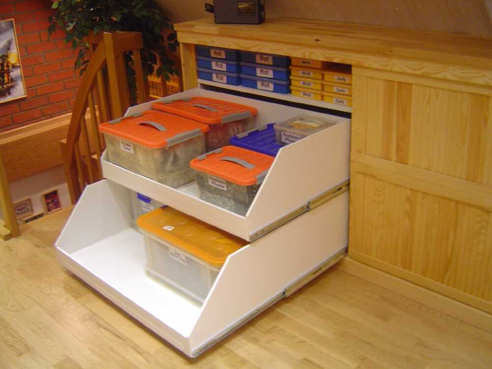 Mehrstufiges Aufbewahrungssystem mit transparenten Boxen mit orange Deckeln vor Holzschrank.
