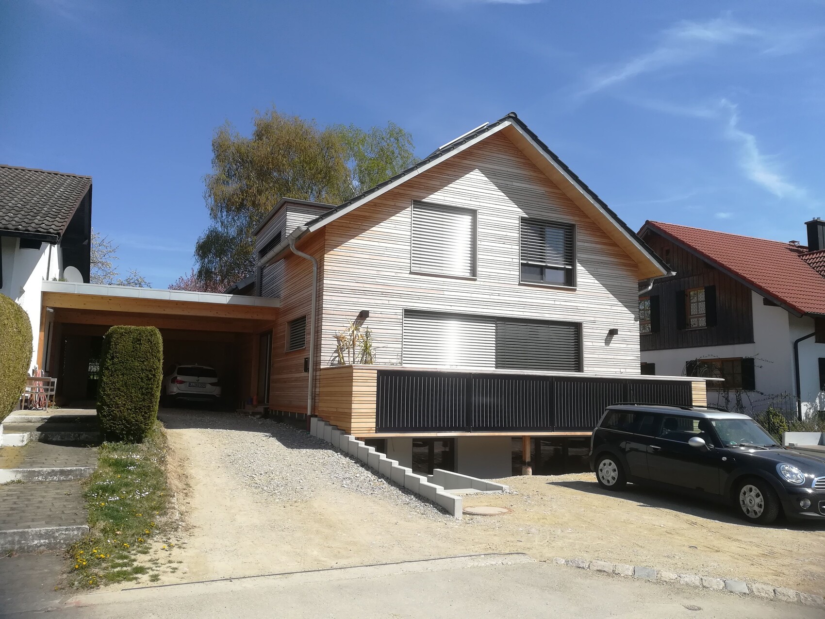 Modernes Haus mit Holzverkleidung, Carport links mit Auto, davor blauer Himmel