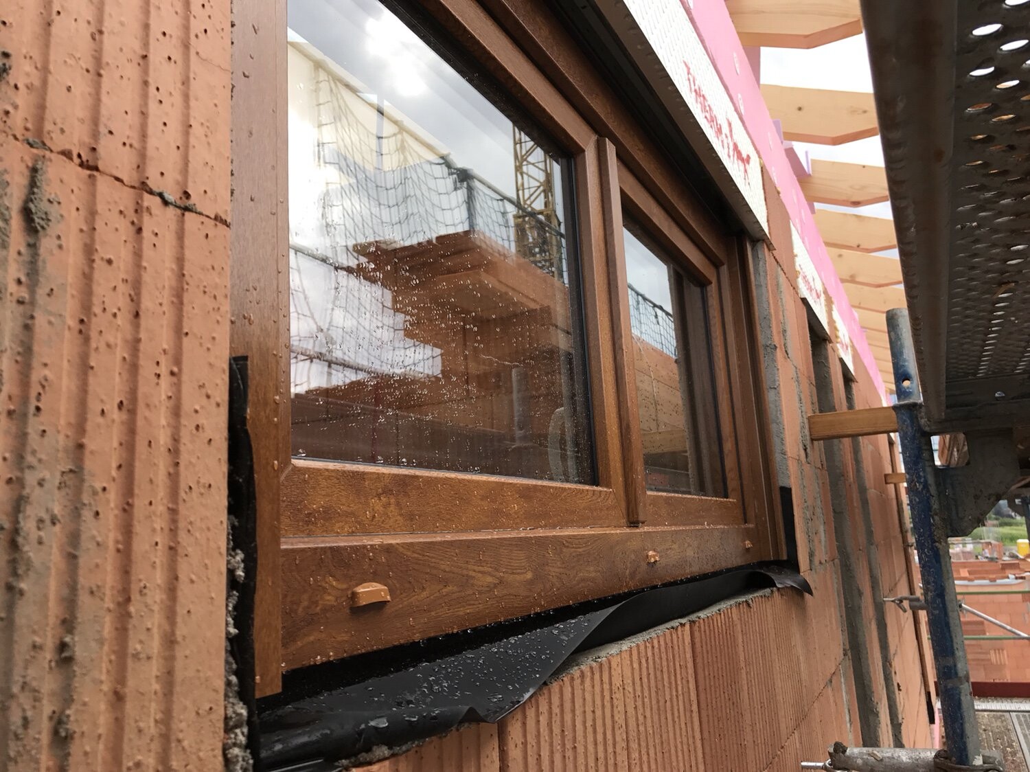 Außenansicht eines Neubauhauses: braune Holzfensterrahmen, Backsteinwand, Gerüst.