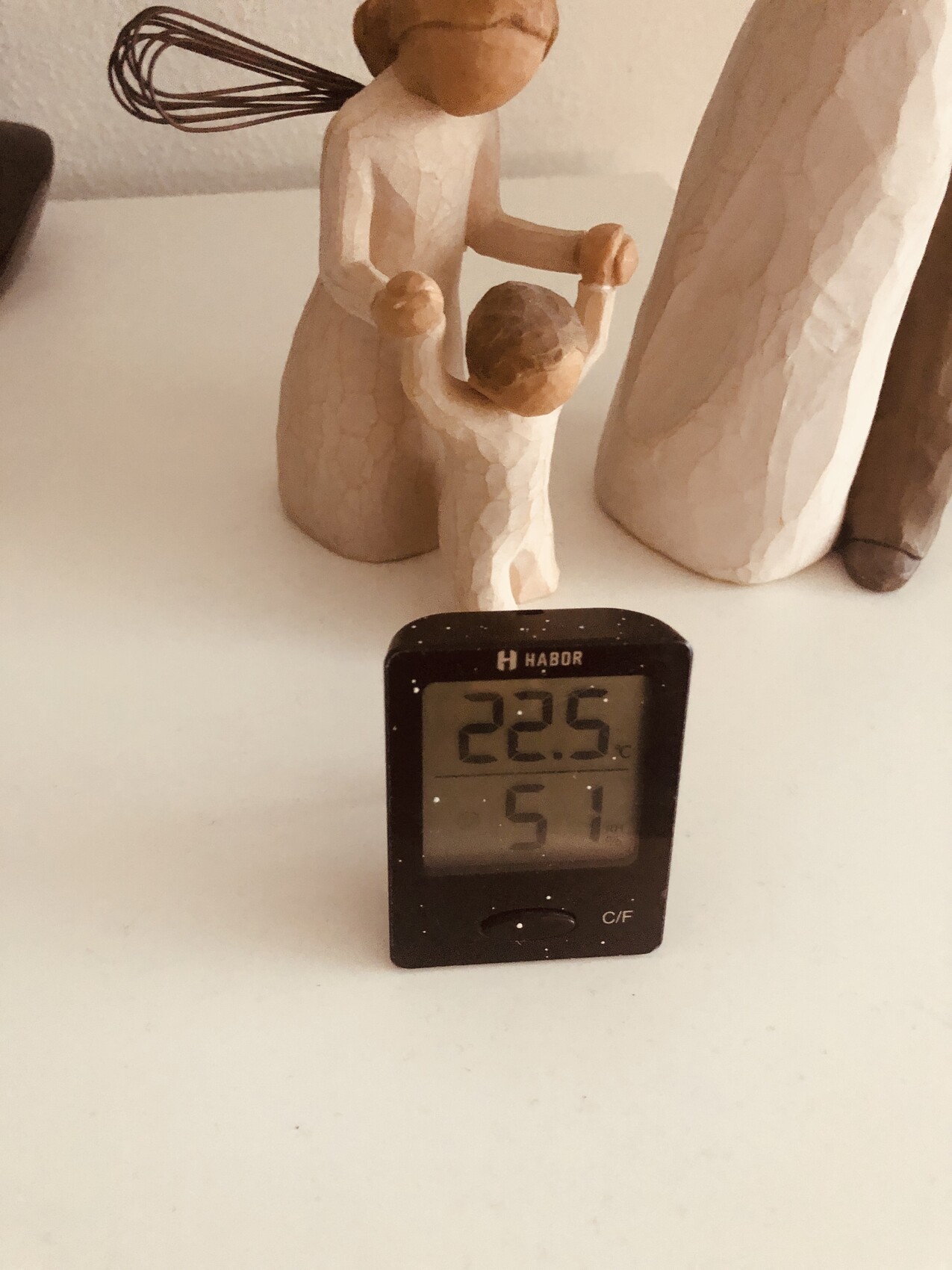Holzfigurengruppe: Mutter hält Kind; daneben digitales Thermometer zeigt 22,5°C und 51% Luftfeuchtigkeit