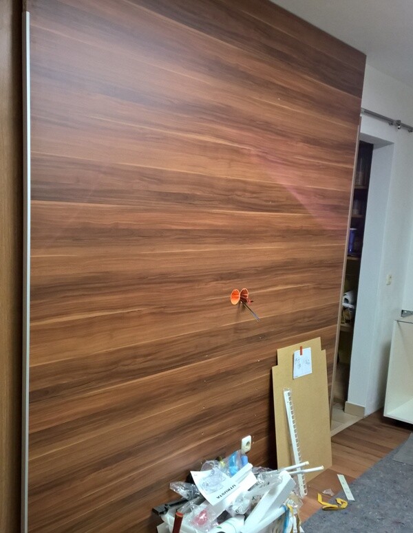 Große Holzschranktür in einer Werkstatt, links Karton, kleines orangenes Bauteil in der Mitte.
