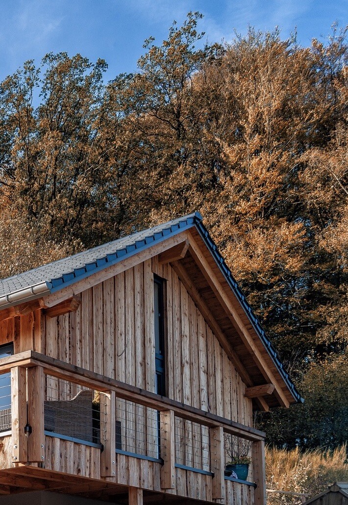 Holzhaus mit Balkon vor Herbstwald und blauem Himmel