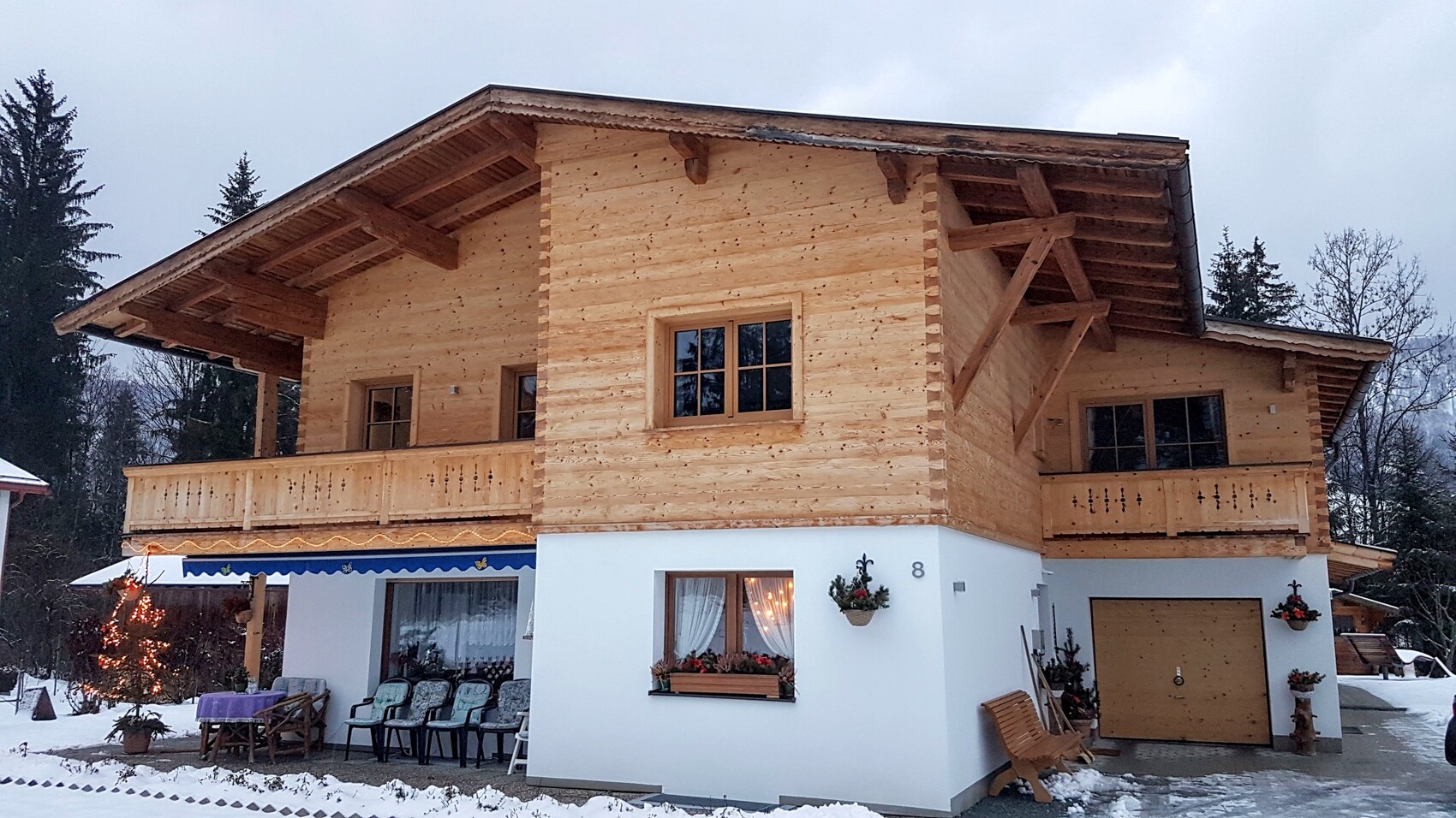 Holz-Chalet mit Balkon, Terrasse und weißem Sockel in verschneiter Winterlandschaft