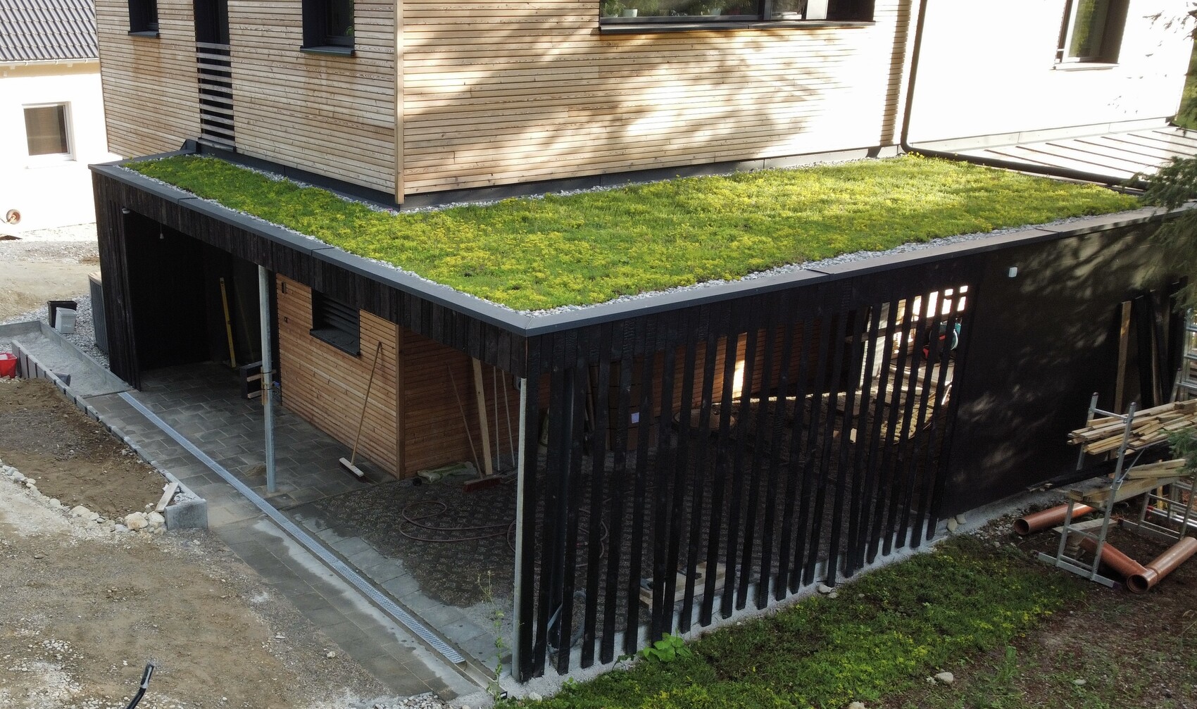 Modernes Haus mit begrüntem Flachdach, Holzverkleidung und offenem Carport.