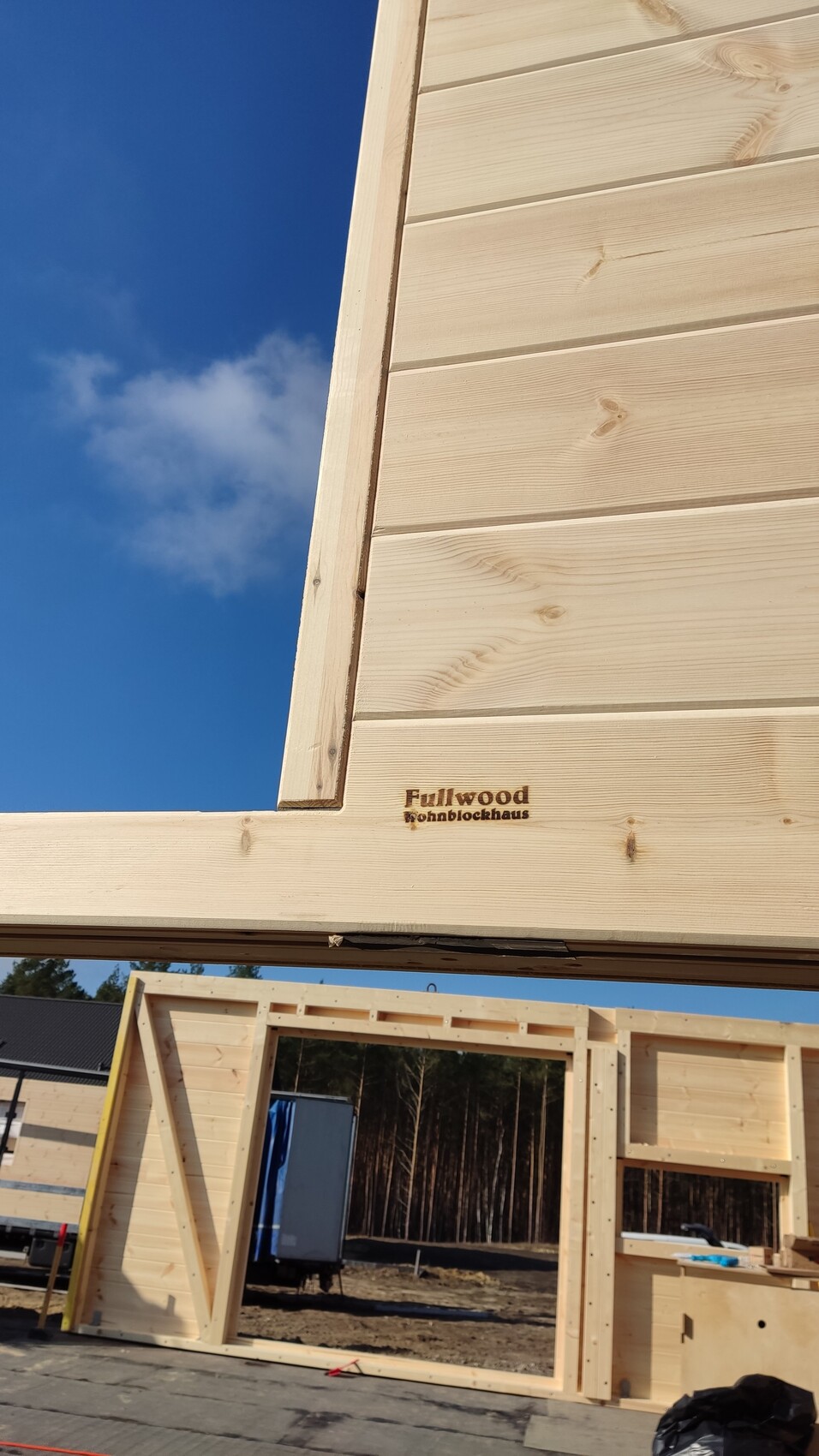 Baustelle mit Holzrahmenbau: Holzwände, blauer Himmel, Logo Fullwood Wohnblockhaus auf Holzbalken