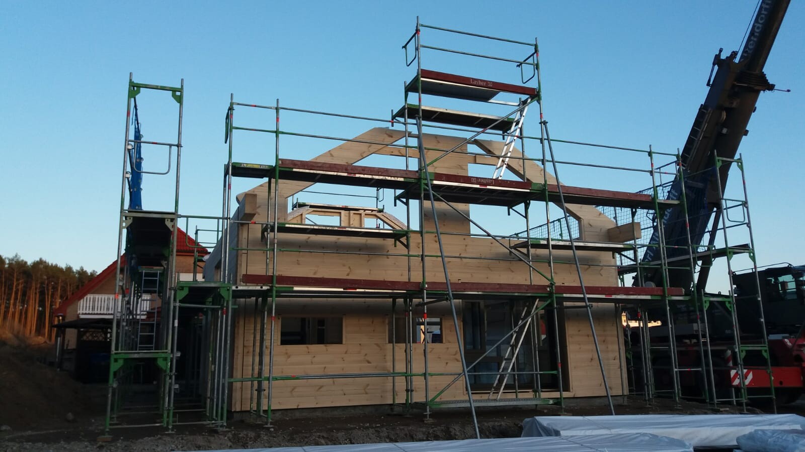 Holzhausbau auf Baustelle mit Gerüst, Kran und sichtbaren Holzwänden.