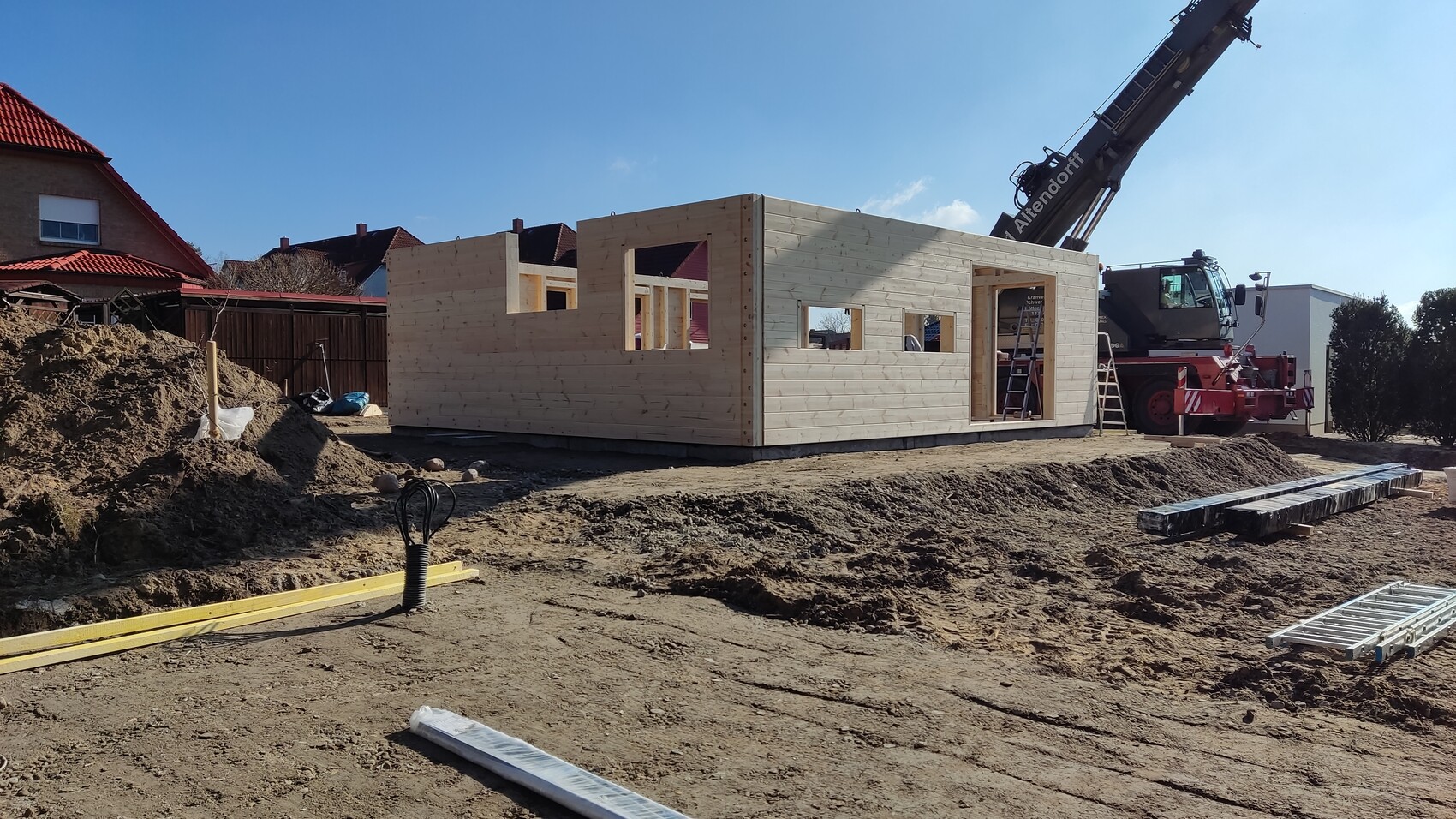 Holzhaus im Rohbau: Holzwandstruktur mit Fensteröffnungen, Baustelle mit Kran im Hintergrund.