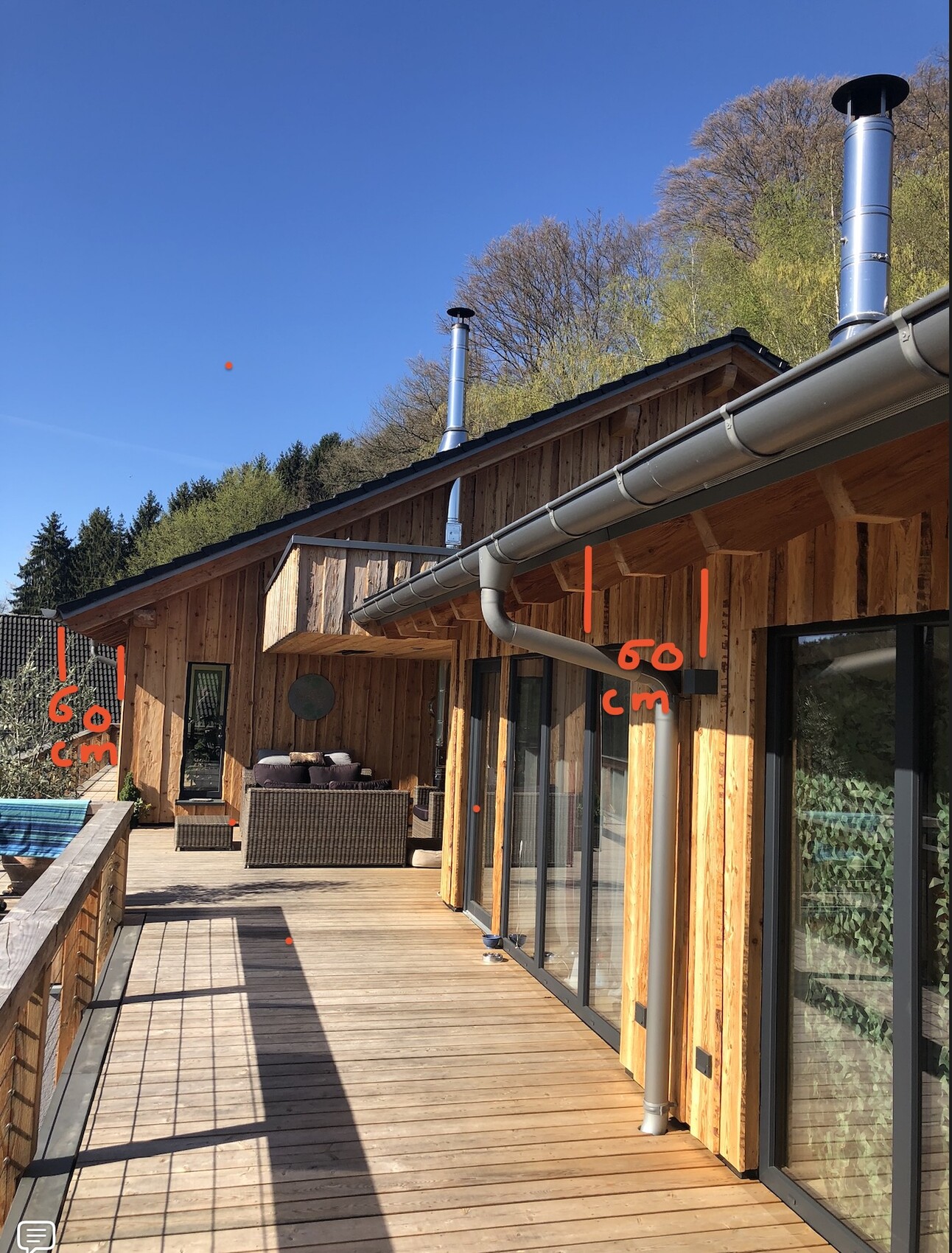 Holzhaus mit großer Terrasse, Glasfronten, Lounge-Möbel und blauem Himmel.