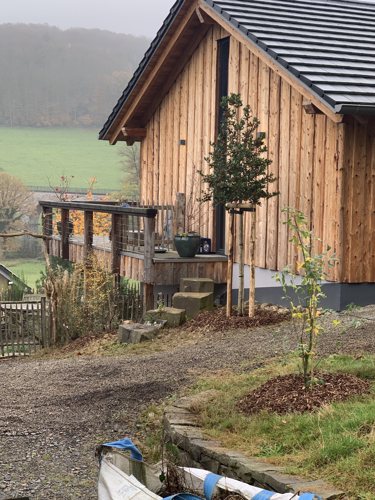 Holzhaus mit Veranda, Topfpflanzen, Kiesweg und ländliches Hanggelände.