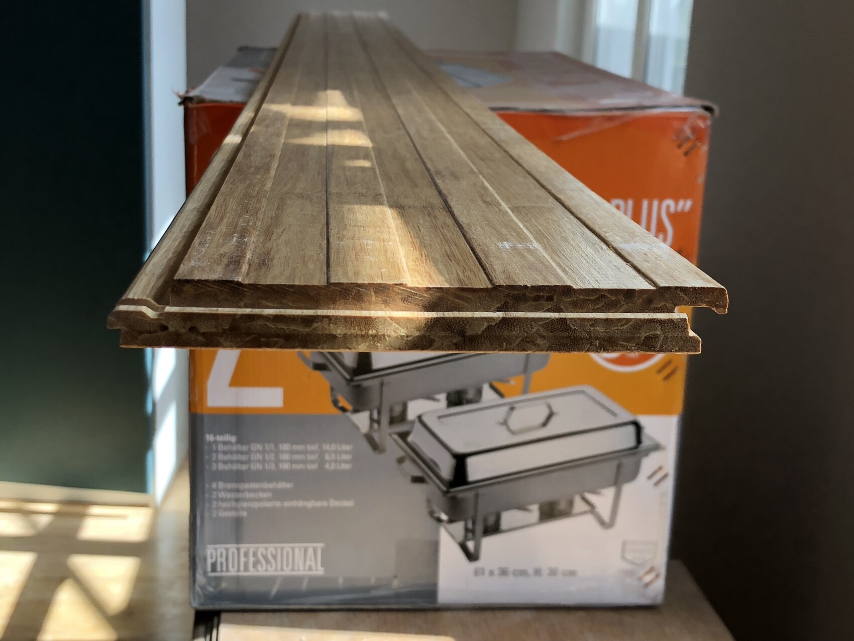 Holzlatten liegen auf einer orangefarbigen Bauverpackung im Innenraum.