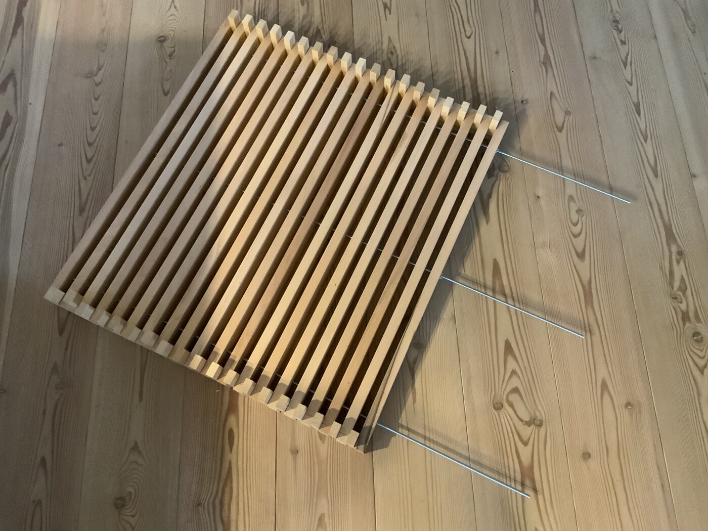 Holzlattenplatte auf Holzboden; drei Metallstangen ragen seitlich heraus.