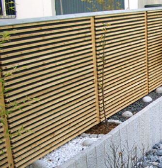 Holzlattenzaun als Sichtschutz im Garten neben einem Kies- und Steinbeet