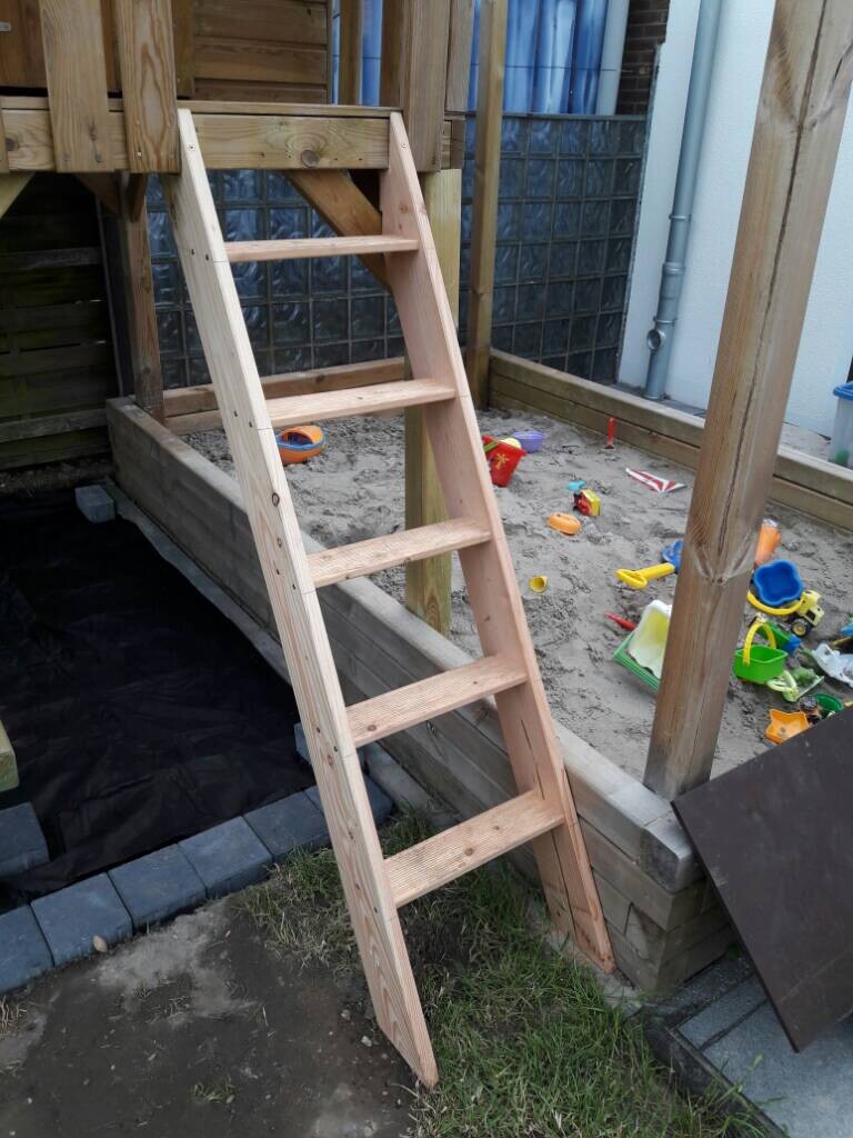 Holzleiter als Treppe zu einem Spielturm im Garten mit Spielzeug drumherum