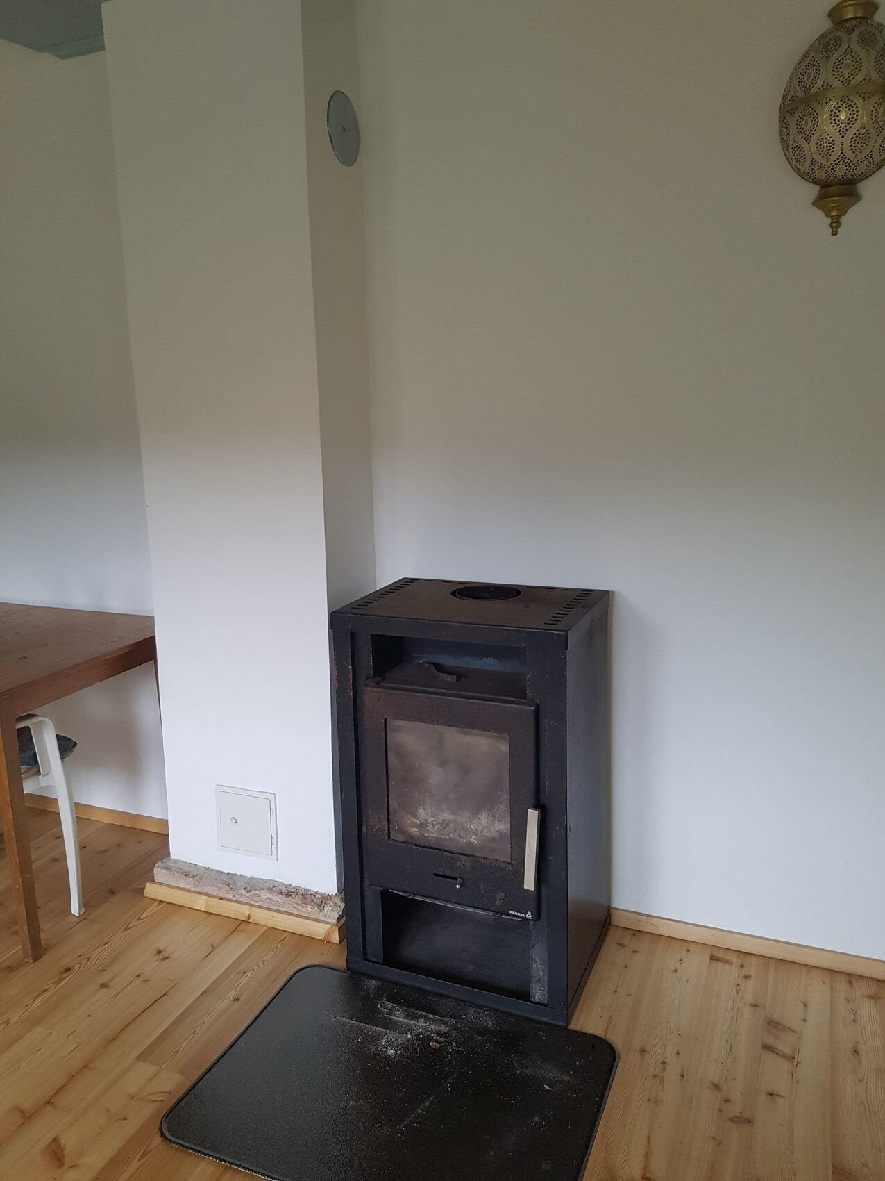 Schwarzer Kaminofen mit Glasfront steht auf hellem Holzboden; davor eine schwarze Matte.