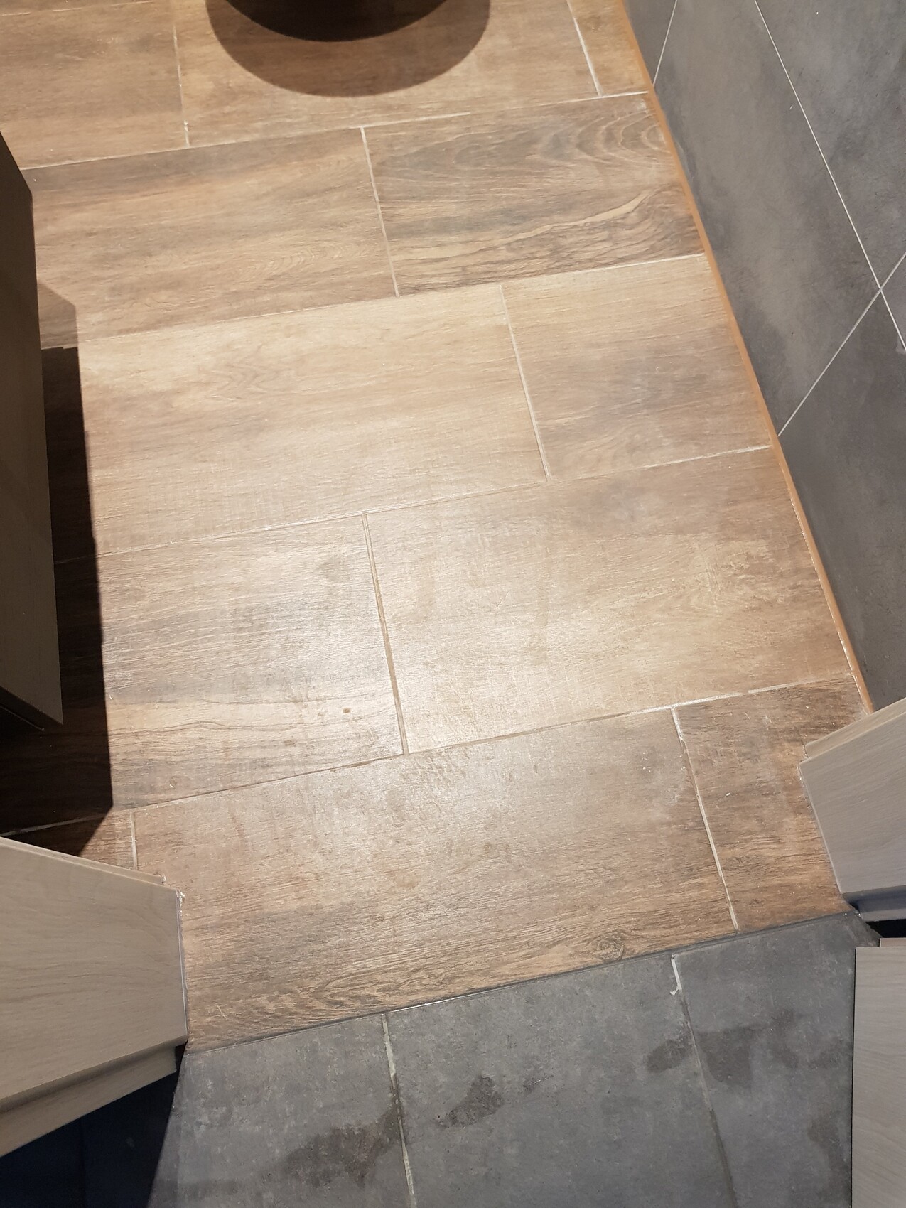 Heller Holzoptik-Fliesenboden mit grauen Randfliesen im Raum.