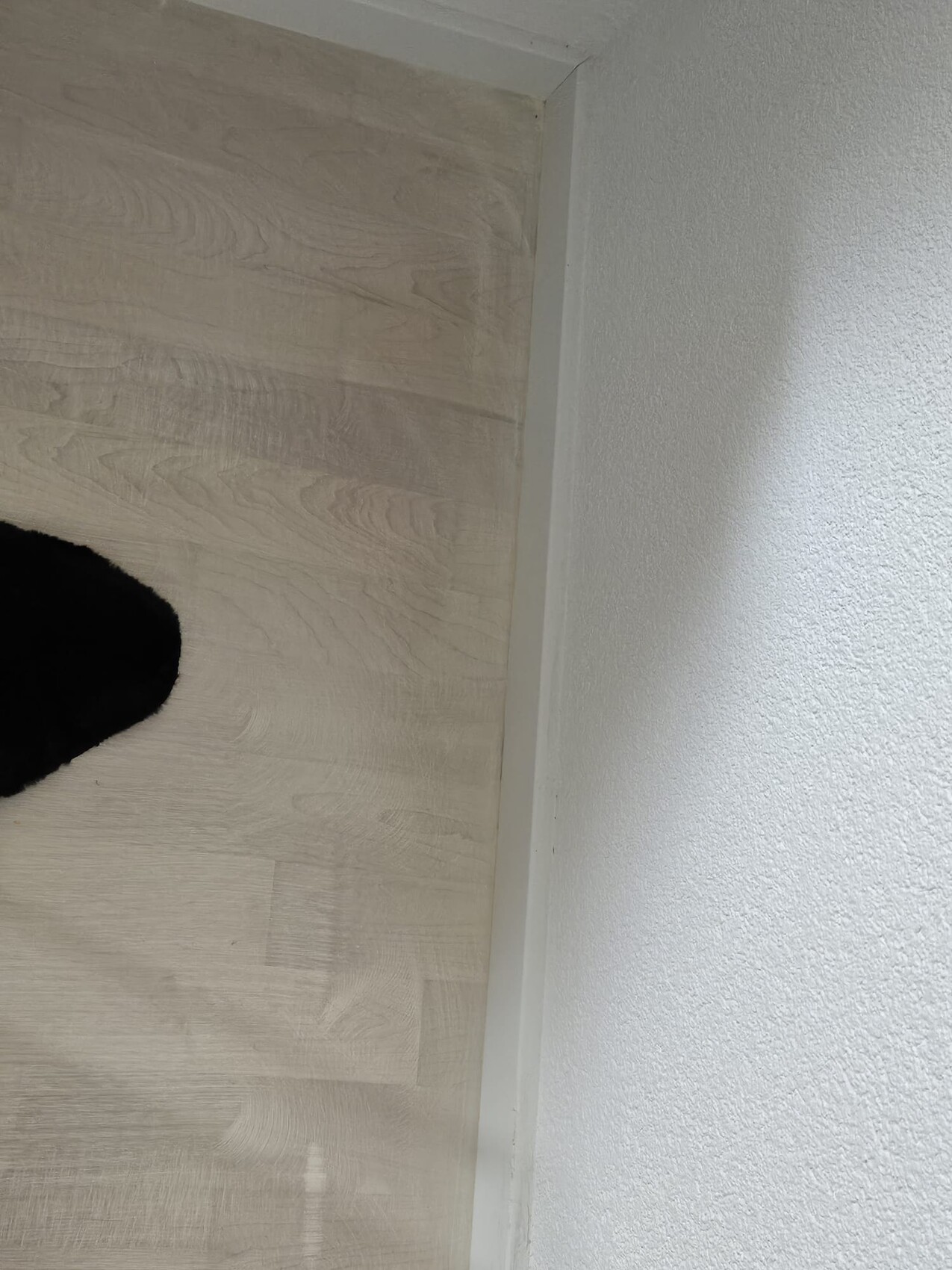 Heller Holzoptik-Bodenbelag in Innenraum, Ecke mit Sockelleiste und weißen Wänden.