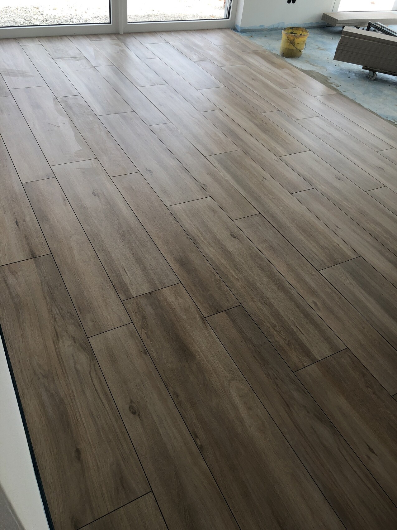 Neu verlegter Holzoptik-Laminatboden in heller Brauntönung; Baustellenutensilien am Rand.
