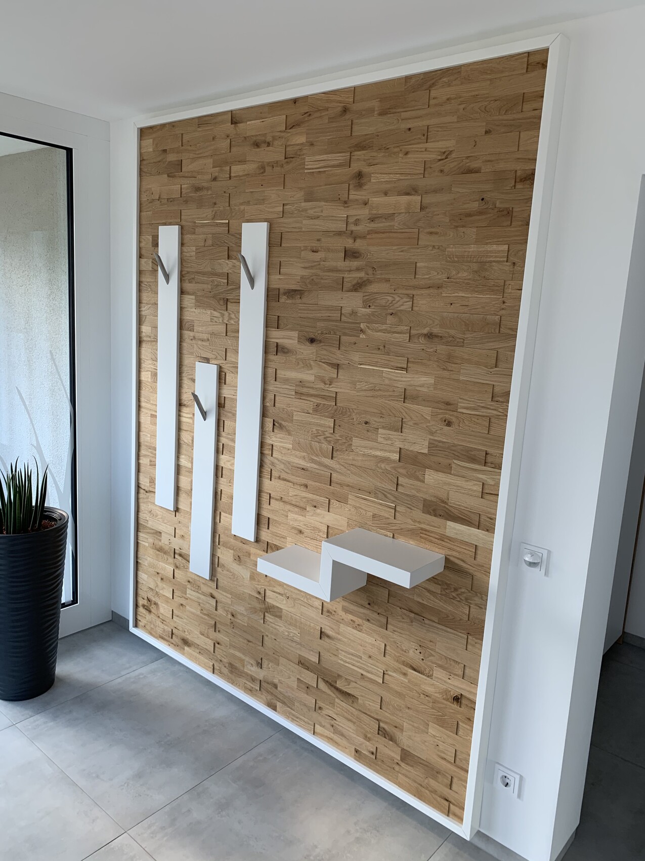 Moderne Holzpaneelwand mit drei weißen Wandleisten mit Metallhaken und einer weißen Ablage.