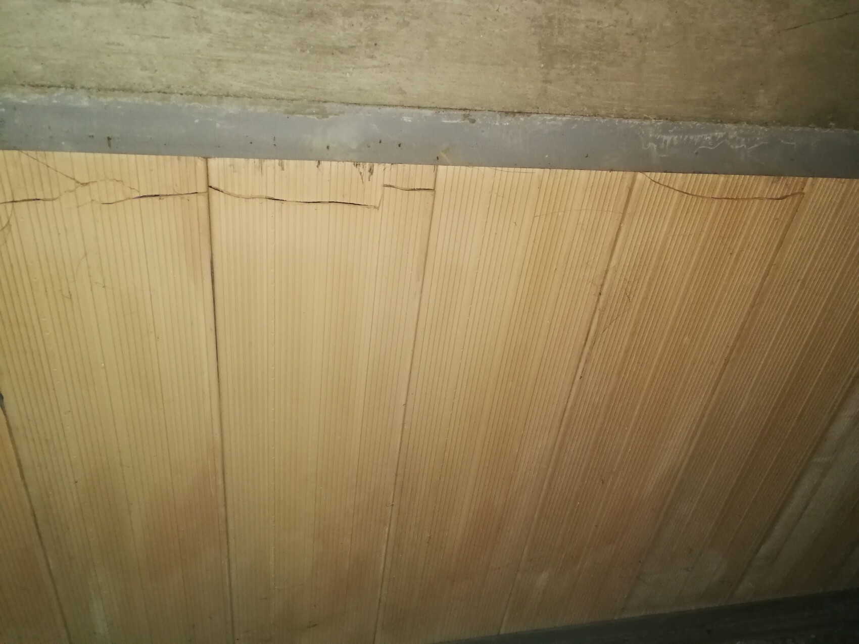 Nahaufnahme von Holzpaneelen mit vertikalen Nutleisten und einer Betonkante oben