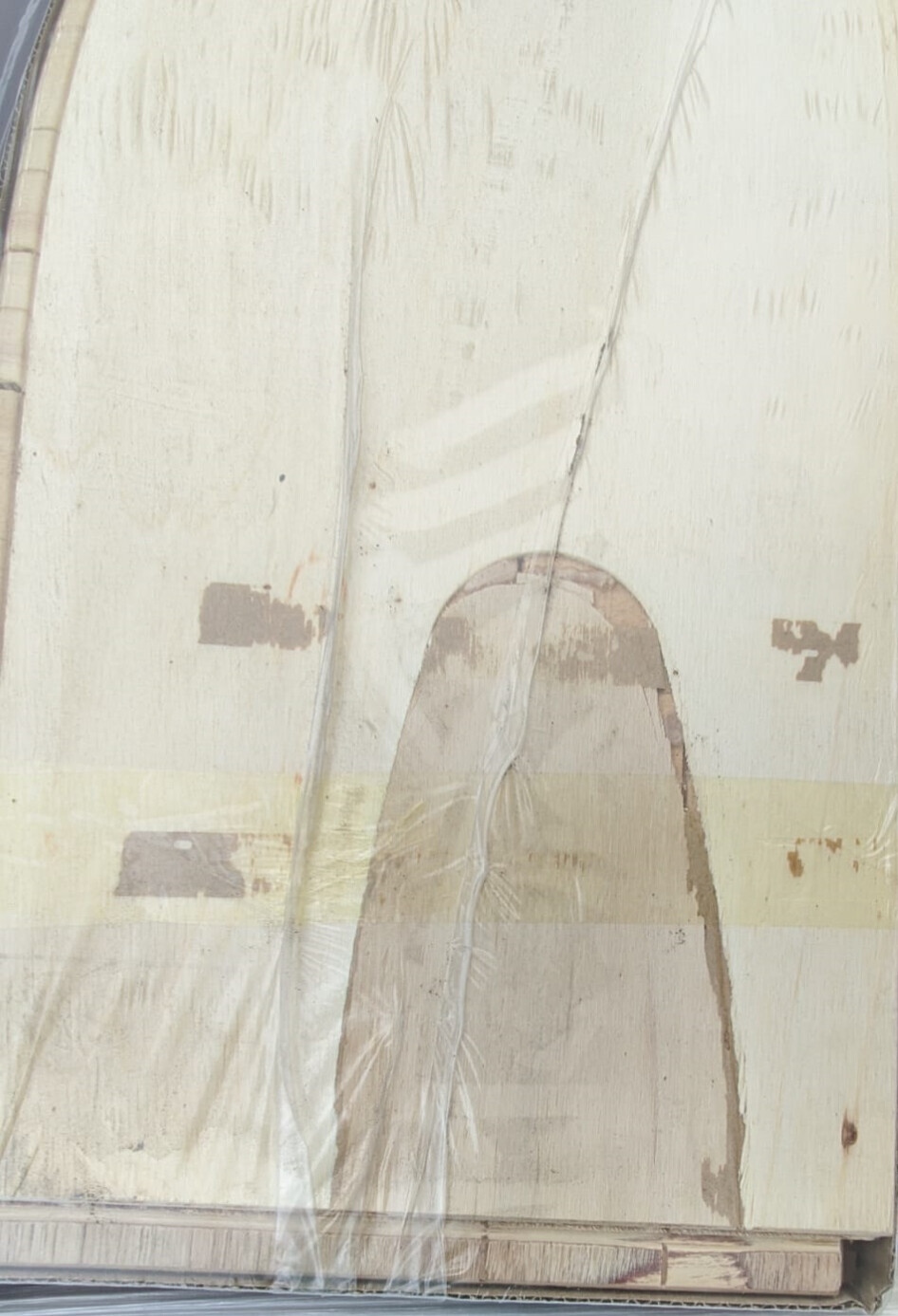 Helles Holzbrett unter Plastikfolie, mit Klebeband und rundem Ausschnitt.