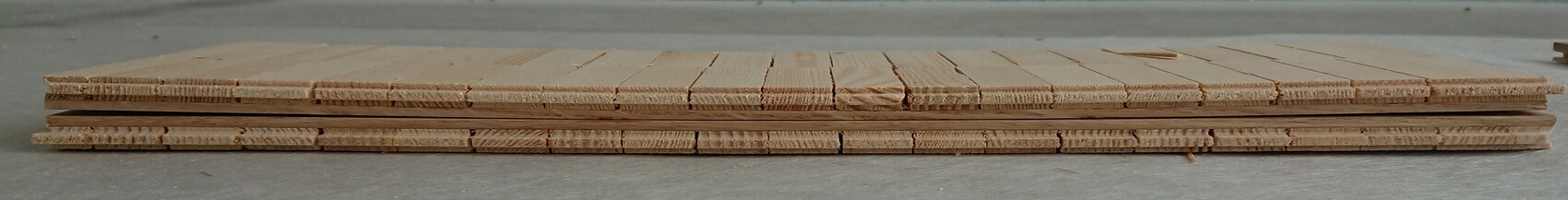 Mehrfach gestapelte helle Holzlatten liegen flach auf dem Boden.