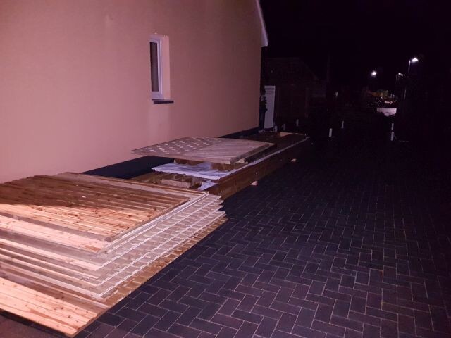 Außenansicht eines Hauses mit gestapelten Holzplatten im Terrassenbereich bei Nacht