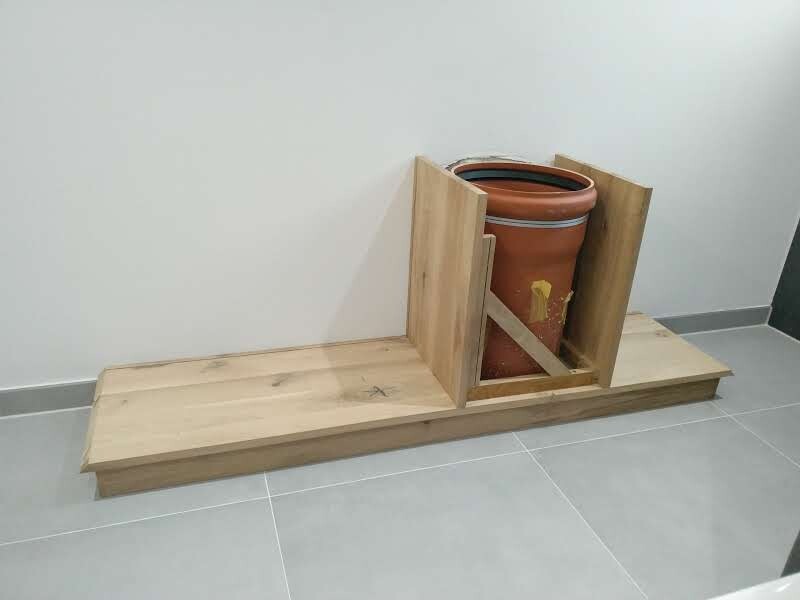 Holzplattform mit Holzkasten, Terracotta-Topf darin auf Fliesenboden.