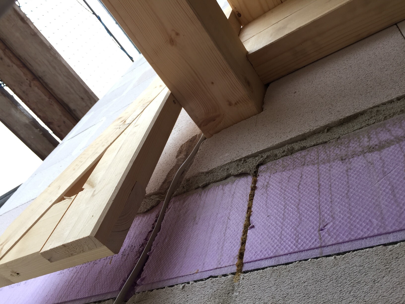 Nahaufnahme von Holzrahmen, rosa Dämmplatten und Mörtel an der Außenwand.